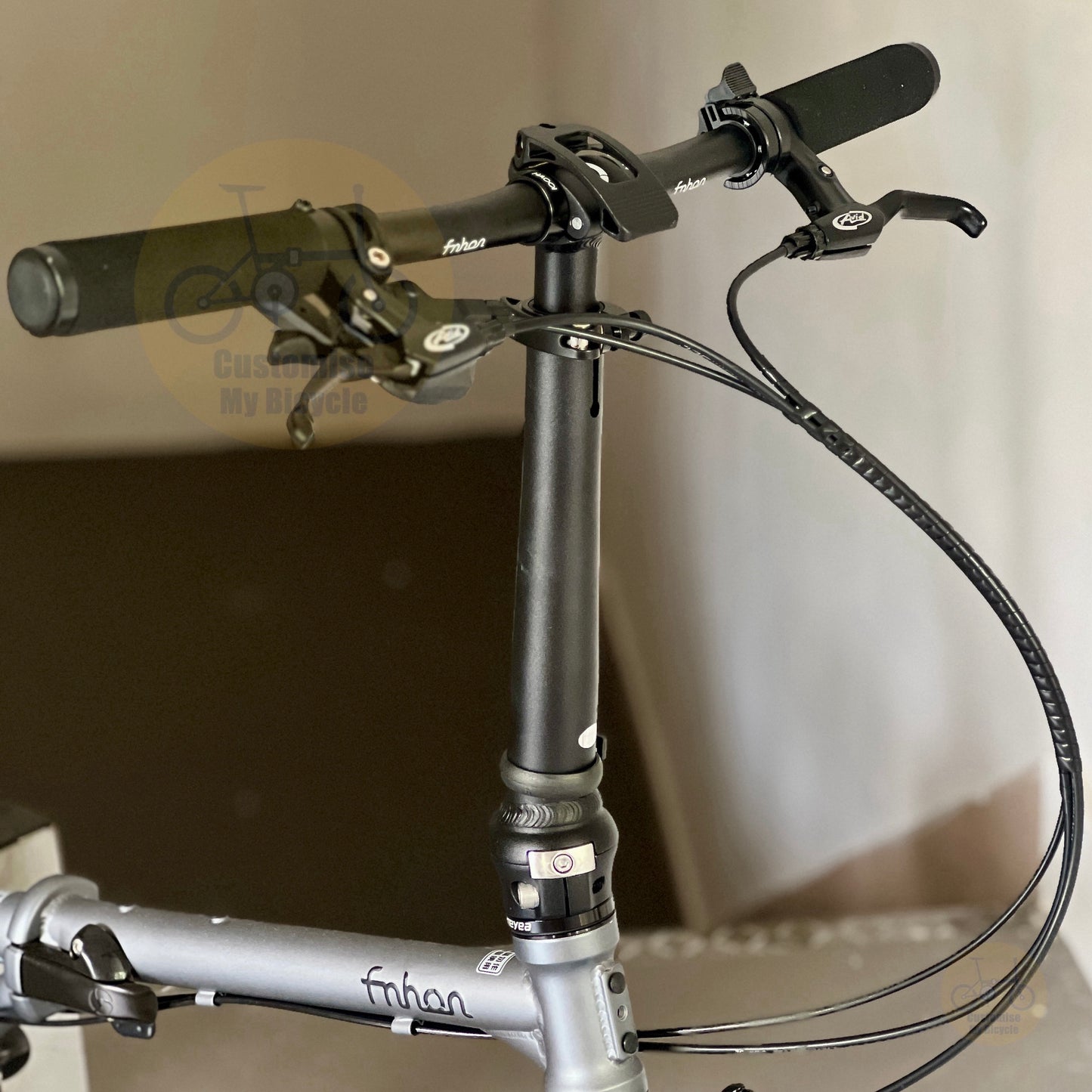 Close-up of a folding bicycle handlebar and stem assembly, showing black grips, brake levers, cables, and a silver frame with 'fabian' branding.