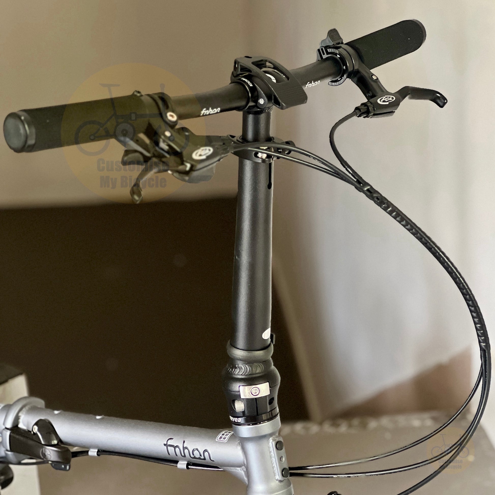 Close-up of a folding bicycle handlebar and stem assembly, showing black grips, brake levers, cables, and a silver frame with 'fabian' branding.