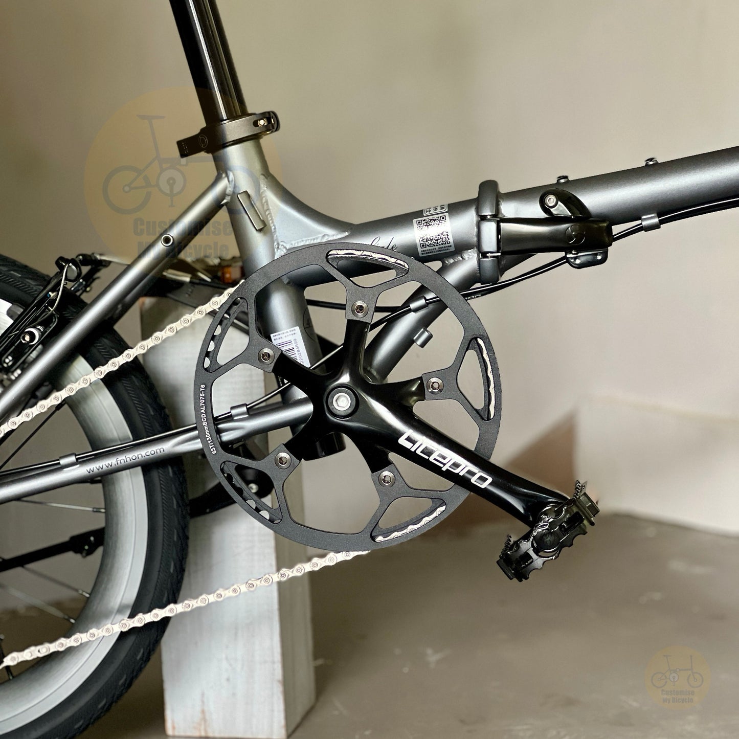 Close-up of a folding bicycle crankset with a black chainring and black pedal arm, attached to a matte gray frame. The brand name 'LIFETO' is visible on the crank arm.