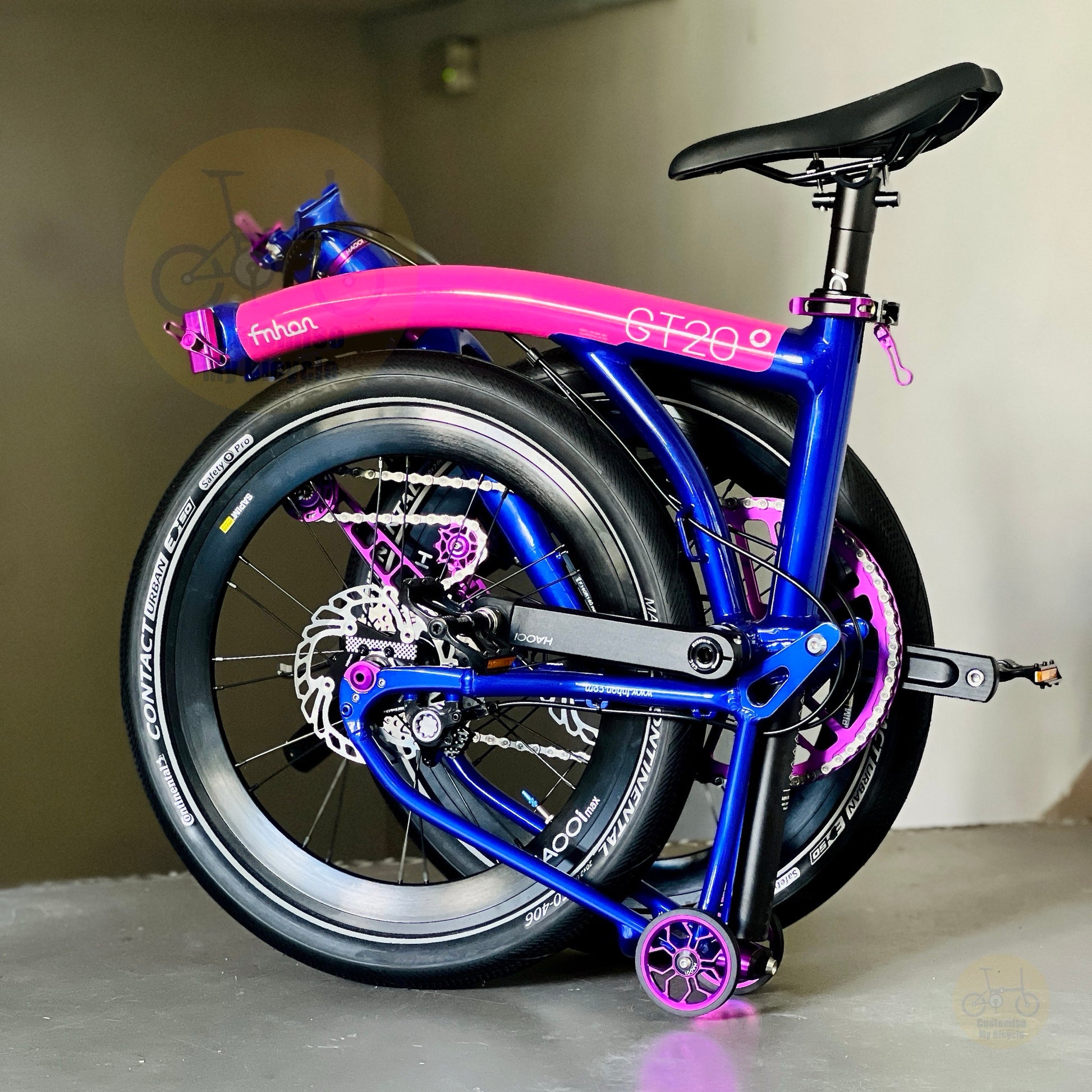 A folded bicycle with a bright blue frame and vivid pink fenders, shown standing indoors on its rear wheel. The bike has visible branding including 'fnhon' on the top tube and 'Continental' on the tire sidewall.