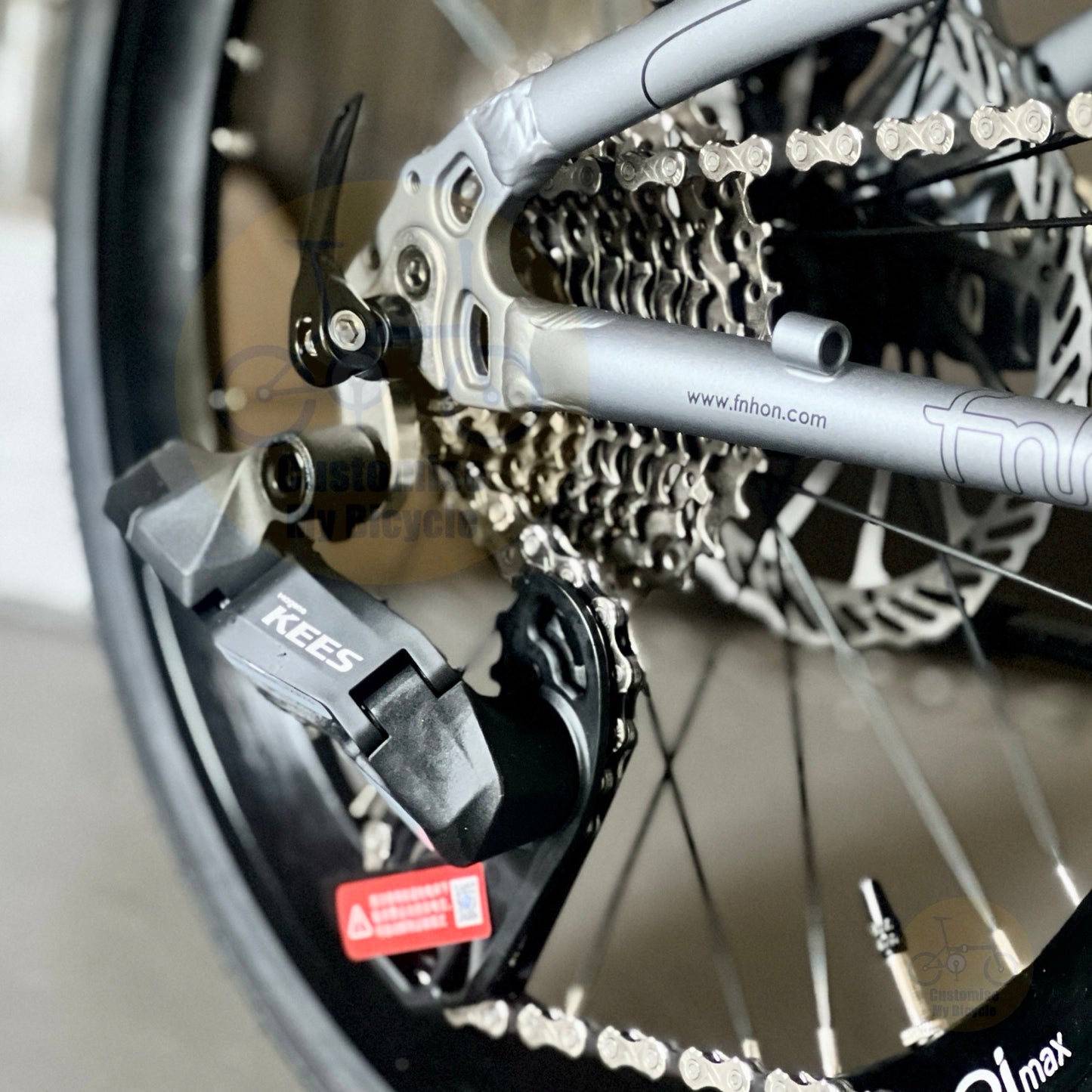 Close-up of a bicycle rear derailleur system with a black KEEPS brand brake/derailleur component, silver chainring, cassette, and part of the frame. A faint website watermark is visible across the image.