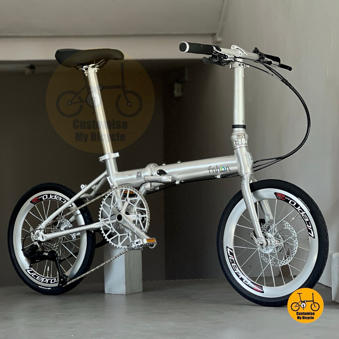 Lower front profile of Fnhon Zephyr 18-inch folding bike in polished silver, displayed on wooden deck with city skyline at sunset.
